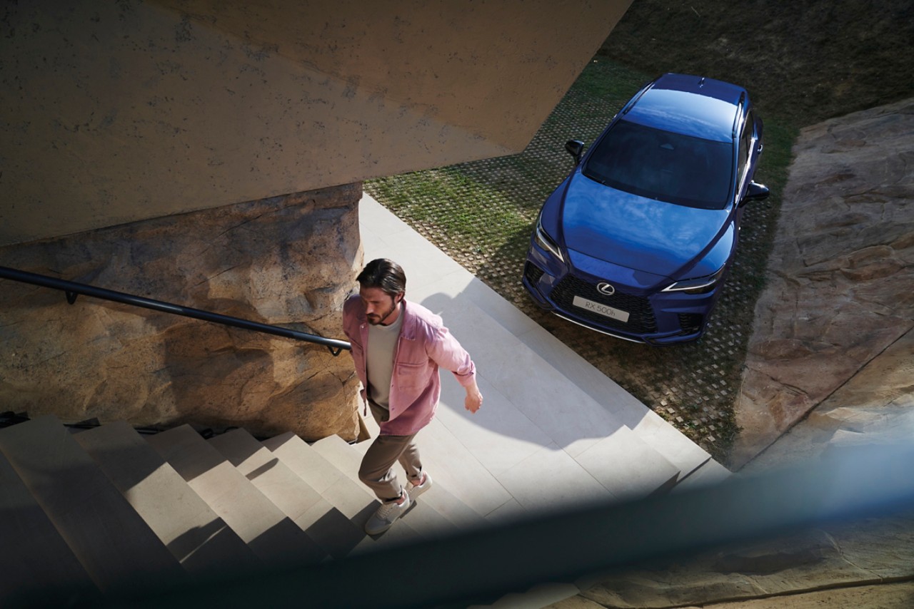 A person walking up steps next to a blue Lexus RX 500h.